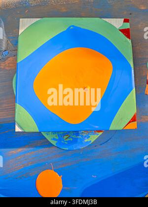 Abstract painting with bold orange, blue, and green swirls on canvas. Paint drips and splatters add texture Stock Photo