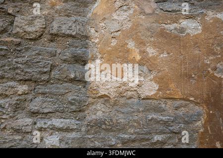 Full frame background texture of an old rustic stone wall showing peeling render and exposed weathered rock beneath. Stock Photo