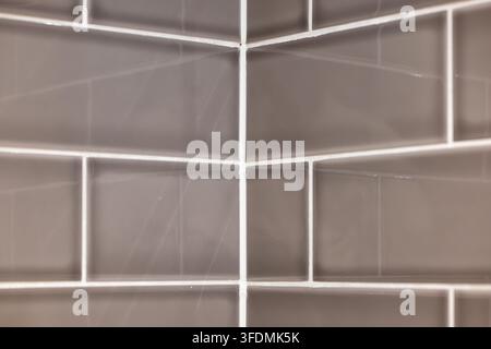 Abstract close up shot of glossy grey subway tiles meeting at an inside wall corner with clean white grouting. Stock Photo