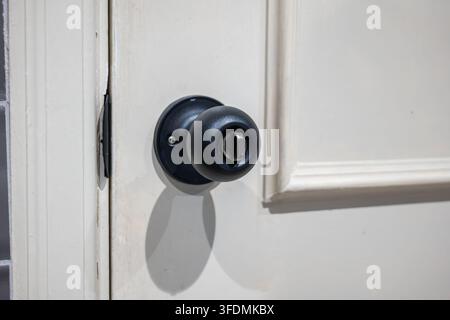 Detailed close up of a round matte black door handle with a privacy lock on a white panel door. Stock Photo