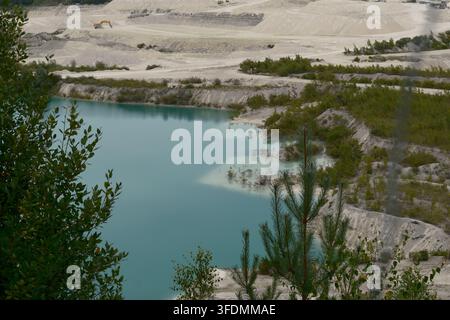 A turquoise meltwater lake in the Faxe limestone quarry, with excavation terraces and machinery on the far side, Faxe, Zealand, Denmark, August. Stock Photo