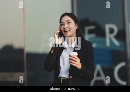 Business woman checks phone in front of modern building during the day Stock Photo
