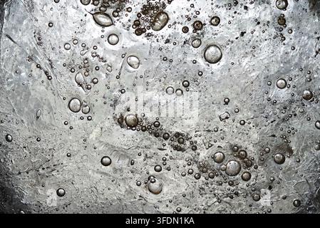 A metallic surface with a reflective, textured appearance features numerous bubble-like formations encapsulated within it. The surface has a silvery s Stock Photo
