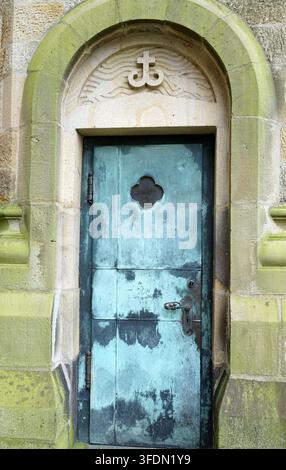 A weathered bronze door of a church set in a stone archway, covered with green patina. The rectangular door features a small, clover-shaped window and Stock Photo