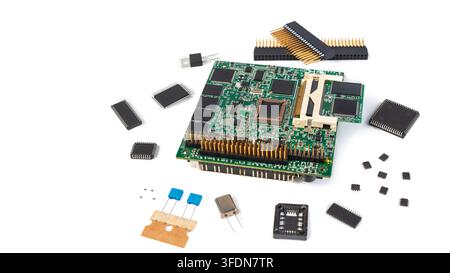 Different electronic parts lay on a white surface, including a circuit board in the middle and small chips around it. Stock Photo