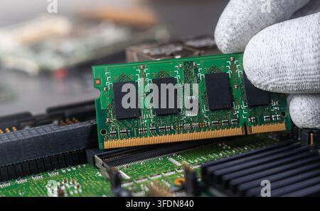 A person works on putting computer memory into a circuit board at a tech repair shop. Tools and other parts are visible in the workspace. Stock Photo