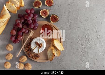 Cheese plate, still life of seasonal wine snacks. Camembert or brie cheese, fresh figs, grapes, baguette, walnuts and honey on cutting board on a gray Stock Photo