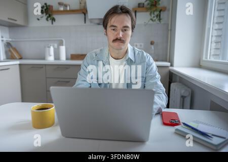 Concentrated man using a laptop to work from home. Thoughtful man looking at computer screen in the kitchen Stock Photo