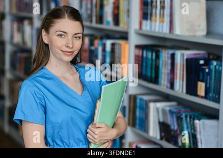 Caucasian female medical student holds textbooks and a notebook while preparing for classes and developing professional knowledge in a university libr Stock Photo