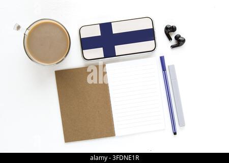 Cup of coffee, smartphone with finland flag on screen, open notebook, pen, marker and wireless earbuds on white desk, concept of learning foreign lang Stock Photo