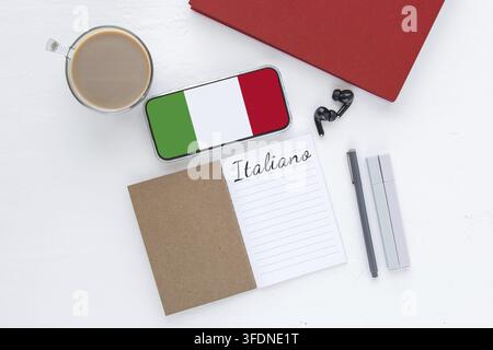 Notebook with word italiano, smartphone with italian flag on screen, coffee cup, earphones and pens on white desk, concept education Stock Photo