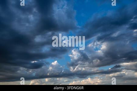 Dramatic moody sky background featuring heavy dark storm clouds against a bright blue atmosphere with sunlight breaking through the layers Stock Photo