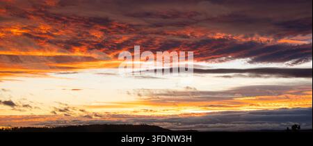 Spectacular fiery sunset with layered clouds in deep orange, red and purple tones, ideal for backgrounds and nature themes. Stock Photo