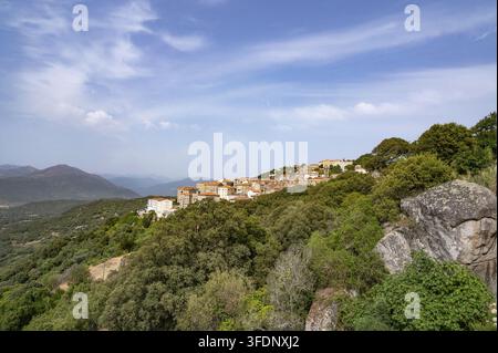 Panoramic view of Sartene's granite houses perched high up on the mountainside over densely overgrown slopes and rocks under a slightly cloudy blue sk Stock Photo