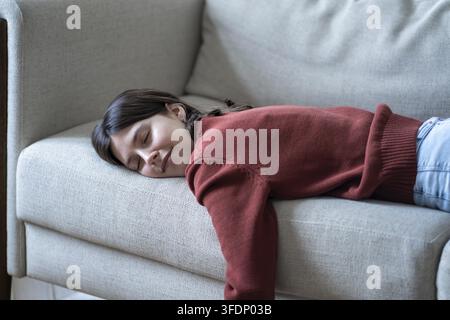 Pleased woman takes nap resting on comfortable sofa feeling carefree, safe. Contented tired girl student taking break after study lying on cozy couch. Stock Photo