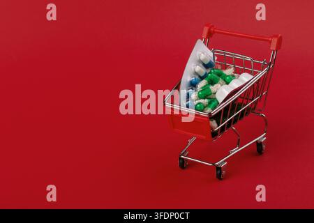 Mini shopping cart filled with blister packs and pill bottles on a vibrant red background, symbolizing healthcare, pharmacy, and medicine retail conce Stock Photo