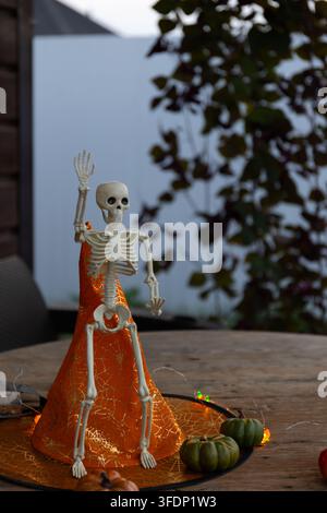 Cozy autumn porch scene features a waving skeleton figurine beside pumpkins, spiderweb fabric, and warm string lights, delivering a welcoming outdoor Stock Photo