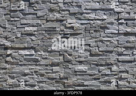 Stone coating wall made of striped stacked bricks of natural gray rocks. External wall covering, background and texture. Stock Photo