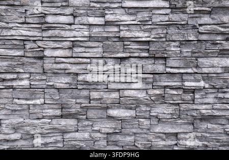 Gray stone coating wall made of striped stacked slabs of natural rocks. Panels for exterior. Background and texture. Stock Photo