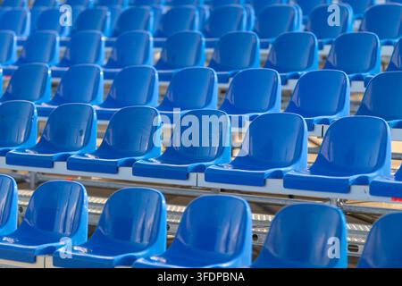 Rows of bright blue seats sit empty ready for fans to arrive and fill the stands, with excitement as the event unfolds under the warm sunlight. Stock Photo