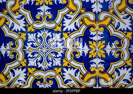 Intricate Portuguese azulejo tile pattern in blue, yellow and white featuring ornate floral and scroll motifs. Close-up of glazed ceramic mosaic used Stock Photo