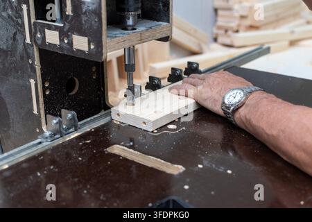Carpenter drilling holes in wooden board on machine rig Stock Photo
