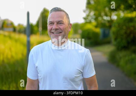 Portrait of smiling senior man outdoors in warm evening sunlight wearing white shirt. Healthy aging and positive mature lifestyle concept in natural s Stock Photo