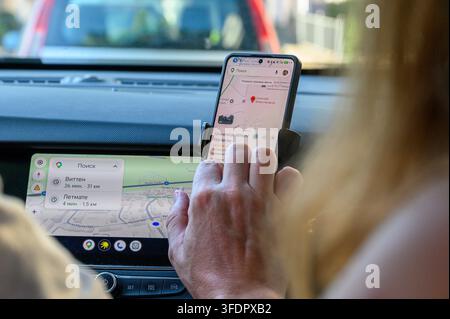 Iserlohn, Germany - August 13, 2026: Person's hand interacting with smartphone displaying navigation while car screen shows a map. Stock Photo
