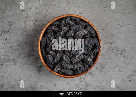 Black raisins in wooden bowl on stone background Stock Photo
