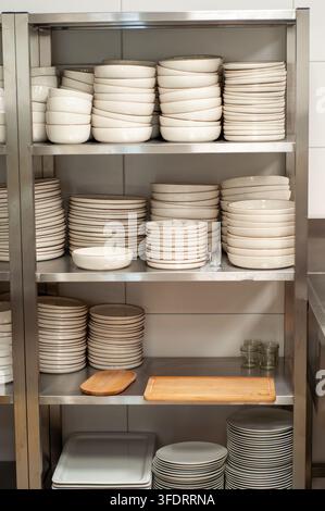 Stacks of white dinnerware on stainless steel shelves Stock Photo