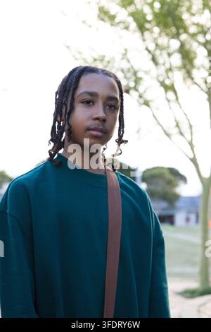 African American teenage male standing in teal crewneck wearing brown bag strap on school campus Stock Photo