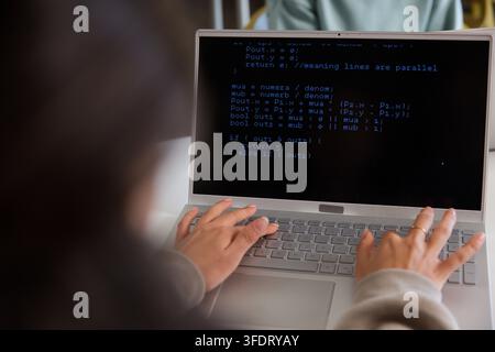 African woman with peer typing code on silver laptop at workspace, beige sleeves, ringed right hand Stock Photo
