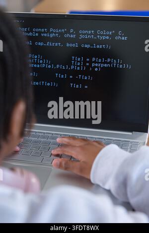 African American youth woman typing code on silver laptop at desk with pink headphones, copy space Stock Photo