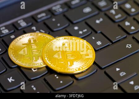 Close-up of two gold-colored coins stamped with bitcoin symbol placed on black laptop keyboard Stock Photo