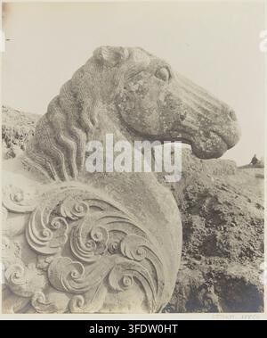 A stone sculpture of a lion's head with a long neck and stylized mane, featuring ornate swirling carvings on its shoulder, positioned in profile facing right, by Victor Segalen, a French photographer, in 1914, as part of the Mission archéologique in China. Stock Photo