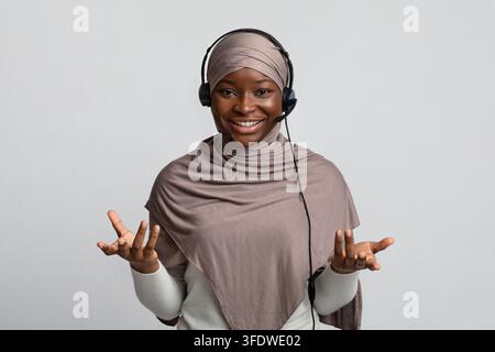 Telemarketin. Black Muslim Woman In Hijab Wearing Headset And Talking At Camera Stock Photo
