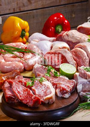 Assorted raw meats for BBQ including picanha, beef steak, chicken, pork, and sausage, arranged on rustic wooden boards with bell peppers. Stock Photo