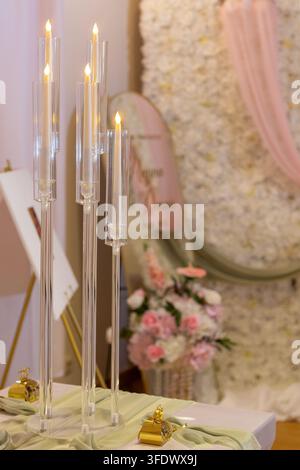 A table is set for a celebration featuring tall glass candle holders with burning candles and a colorful floral arrangement. Soft colors in the backgr Stock Photo