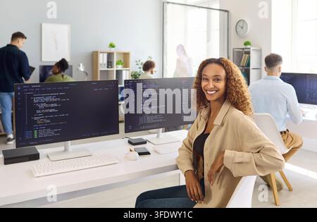 Confident woman programmer at dual monitors in bright collaborative tech office Stock Photo