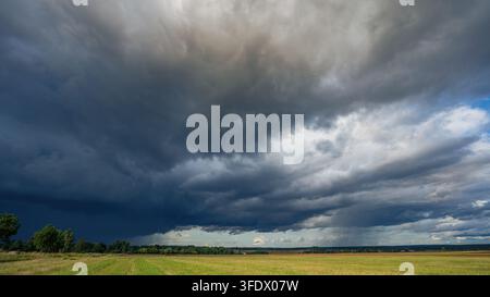 Dramatic storm clouds over a rural agricultural landscape with green and golden fields, dark rain clouds, and a distant tree line under a moody sky Stock Photo