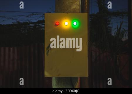 A yellow metal electrical control box mounted on a pole outdoors at night, featuring three illuminated indicator lights in red, yellow, and green. Stock Photo