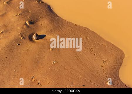 Textured mud puddle with artistic ripples and a small stone at the edge of a clay quarry, showcasing natural patterns and earthy tones in a minimalist Stock Photo
