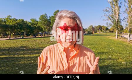 Mature woman wearing star glasses talking outdoors in park Stock Photo