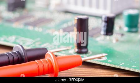 Red and black multimeter probes lying in front of a blurred green electronic circuit board Stock Photo