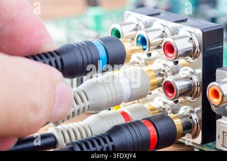 Hand plugging a blue RCA cable into an analog audio-video connector panel on a circuit board Stock Photo