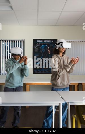 Diverse teens wearing hoodies standing in school lab using white VR headsets, exploring AI poster Stock Photo