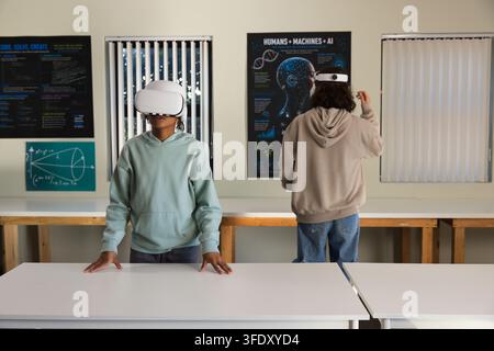 African students wearing hoodies and white VR headsets standing at table in classroom with posters Stock Photo