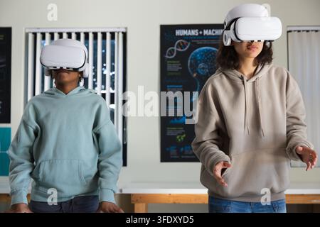 Diverse youths wearing VR headsets at wood table in classroom, exploring Humans+Machines poster Stock Photo