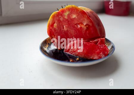 A large, fleshy, sliced ​​tomato on a blue saucer with a gold rim. Stock Photo