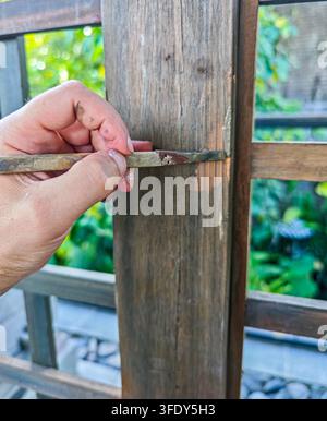 Close-up view of a hand holding a small tool against a wooden fence post Stock Photo